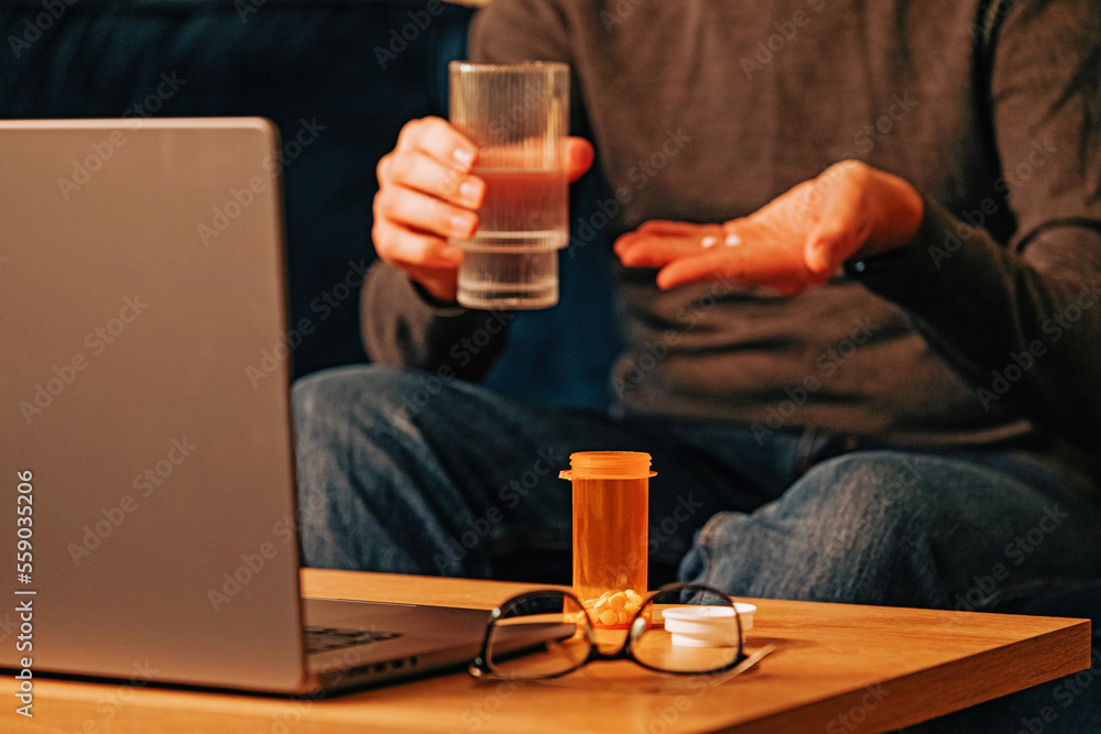 Unrecognizable man taking medicine while working at the laptop. Unrecognizable man taking medicine while working at the laptop.