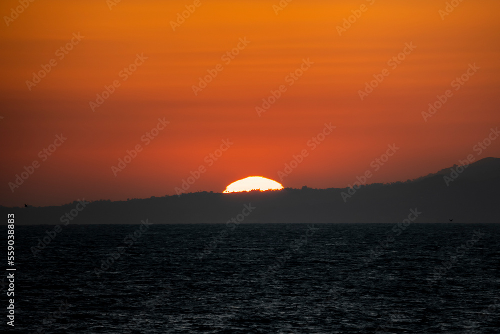 Scenic and idyllic view of seascape and beautiful sun setting down behind silhouette mountain with orange sky in background at Los Angeles Scenic and idyllic view of seascape and beautiful sun setting down behind silhouette mountain with orange sky in background at Los Angeles