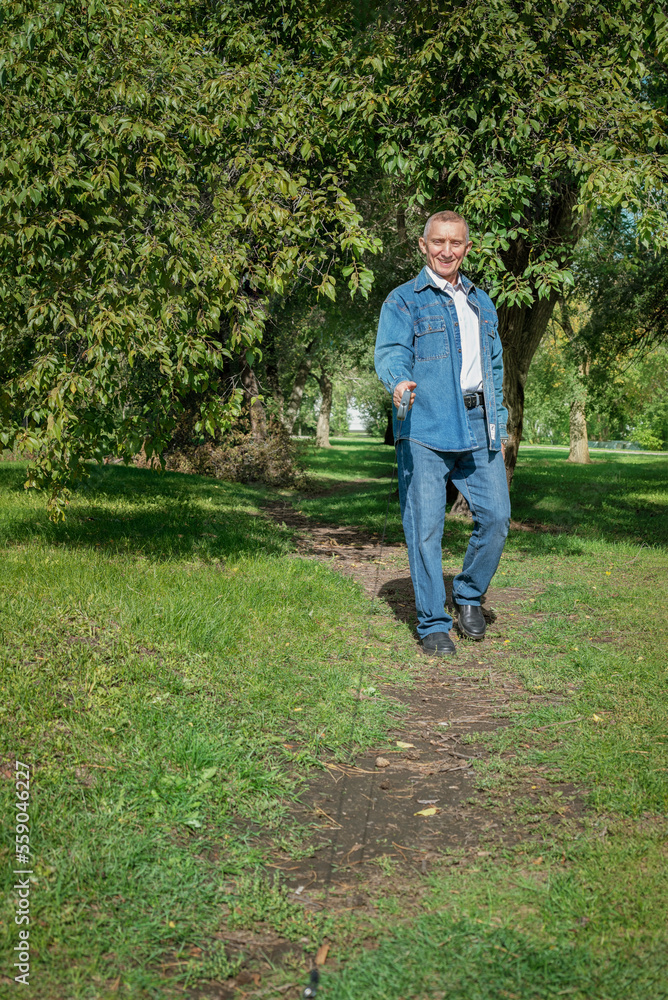 an elderly man walks with a dog in the park, holds a leash and laughs. The dog behind the scenes, selective focus