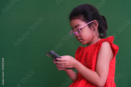 Little girl in her red dress and glasses busy playing game on her gadget photo