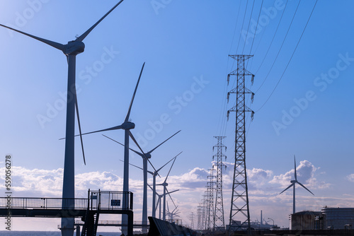 中央の送電線を挟んで風力発電と石油タンクの脱炭素対比の風景