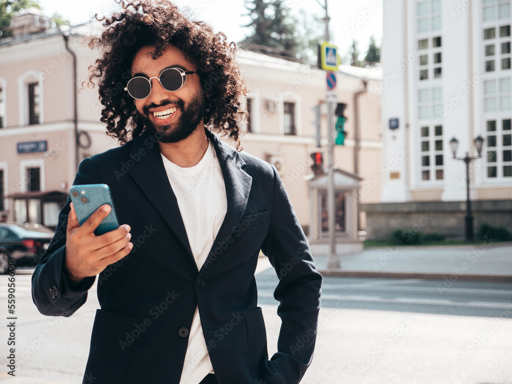 Handsome smiling hipster model.Sexy unshaven Arabian man dressed in summer suit jacket clothes.Fashion male with long curly hairstyle in the street, using smartphone apps, looking at cellphone screen Handsome smiling hipster model.Sexy unshaven Arabian man dressed in summer suit jacket clothes.Fashion male with long curly hairstyle in the street, using smartphone apps, looking at cellphone screen