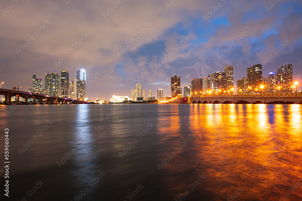 Miami city skyline panorama at night skyscrapers and bridge over sea with reflection