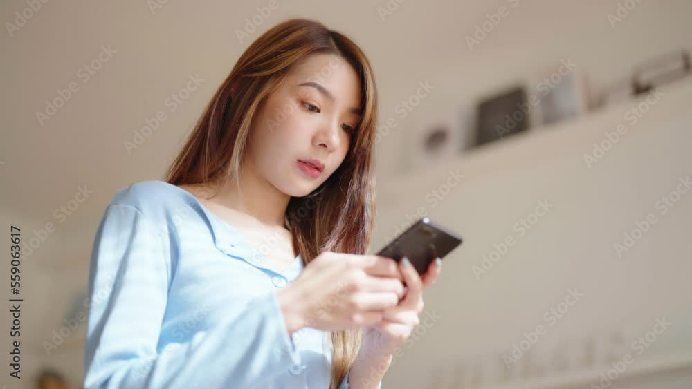Happy young asian woman relax on comfortable couch at home texting messaging on smartphone, smiling girl use cellphone chatting, browse wireless internet on gadget, shopping online from home Happy young asian woman relax on comfortable couch at home texting messaging on smartphone, smiling girl use cellphone chatting, browse wireless internet on gadget, shopping online from home