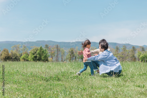 草原・公園で両親に走って抱きつく活発な子供（女の子） 