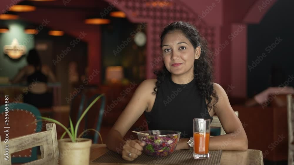 Portrait of smiling young Indian woman eating fresh salad at restaurant. Beautiful Asian girl tasting vegetarian food at cafe. Close Up young female keeping corn on fork indoors.