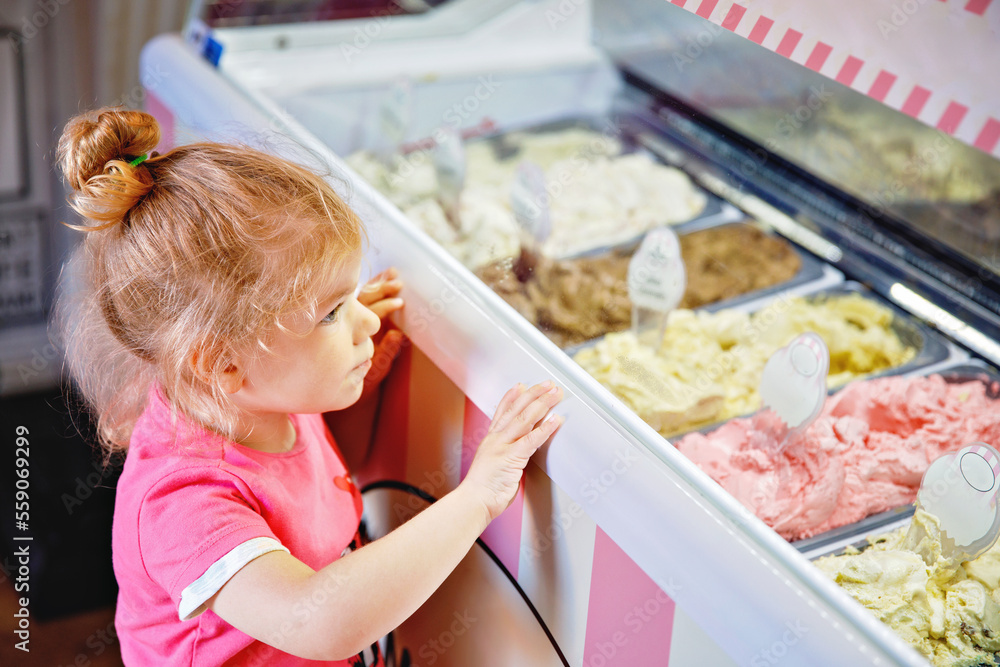 Cute little toddler girl choosing and buying ice cream in a cafe. Happy baby child looking at different sorts of icecream. Sweet home made dessert Cute little toddler girl choosing and buying ice cream in a cafe. Happy baby child looking at different sorts of icecream. Sweet home made dessert