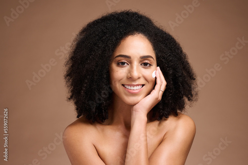 Face, beauty and skincare with a model black woman in studio on a borwn background to apply lotion. Portrait, hand and hair with an attractive young female posing to promote a natural skin product