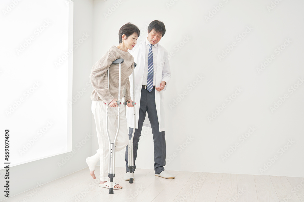 骨折して松葉杖で歩く中年女性 骨折して松葉杖で歩く中年女性