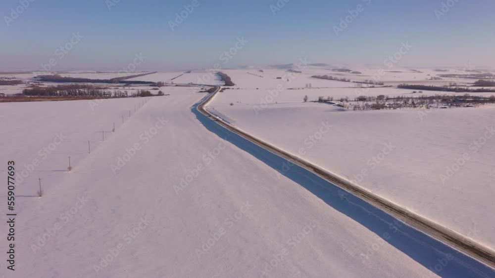 The car drives along the road among the snow-covered fields in winter, aerial photography of the movement