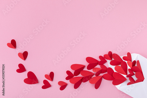 Creative composition on Saint Valentine day. Envelope and paper red hearts for love message on pink background. . photo