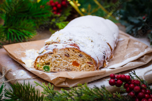 Christmas stollen its a Traditional Dresdner German Christmas cake Stollen with raising, berries and nuts. Sliced stollen on paper and Christmas decoration. Selective focus, shallow depth of field photo