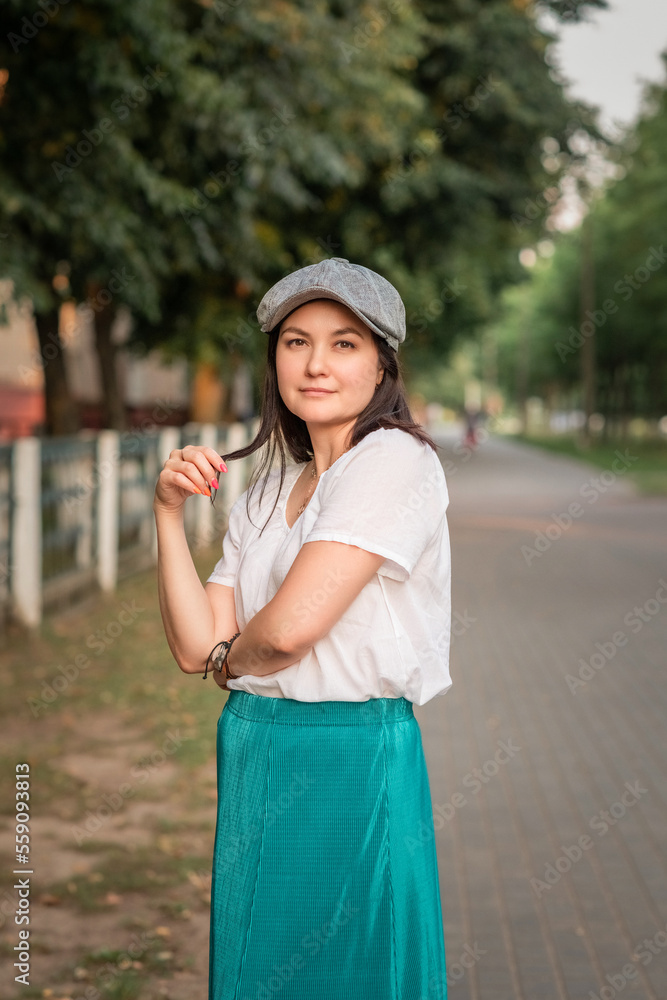 Portrait of a young beautiful dark-haired girl in a cap in a summer park.