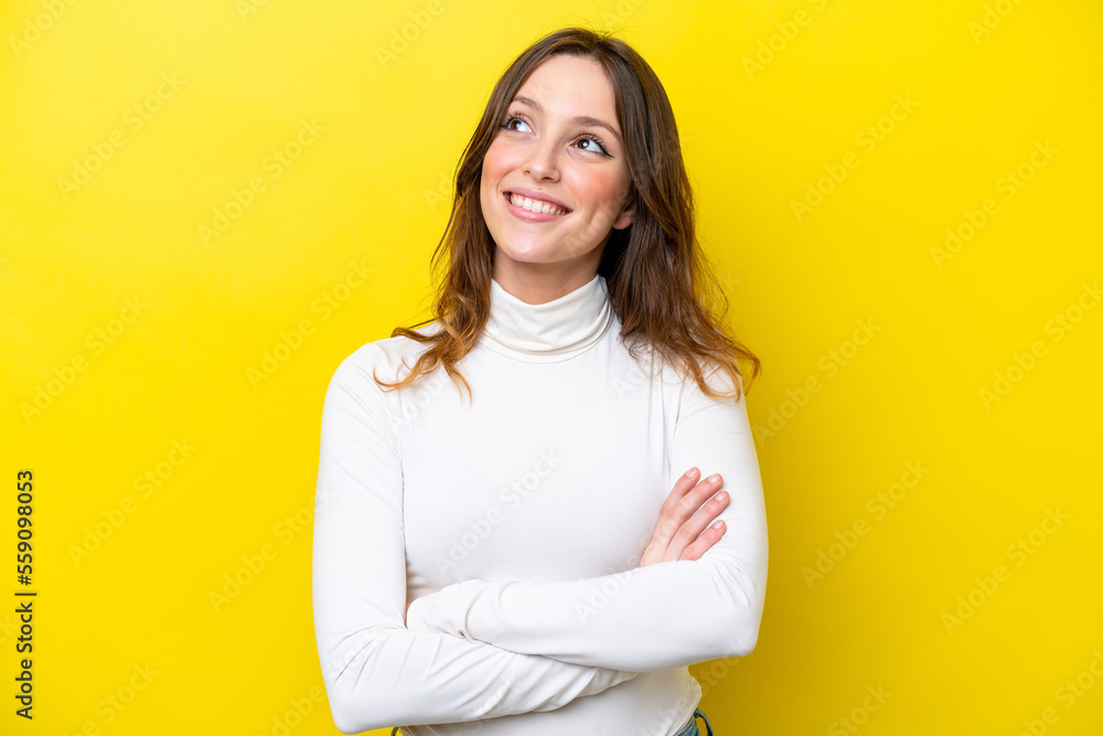 Fototapeta premium Young caucasian woman isolated on yellow background looking up while smiling