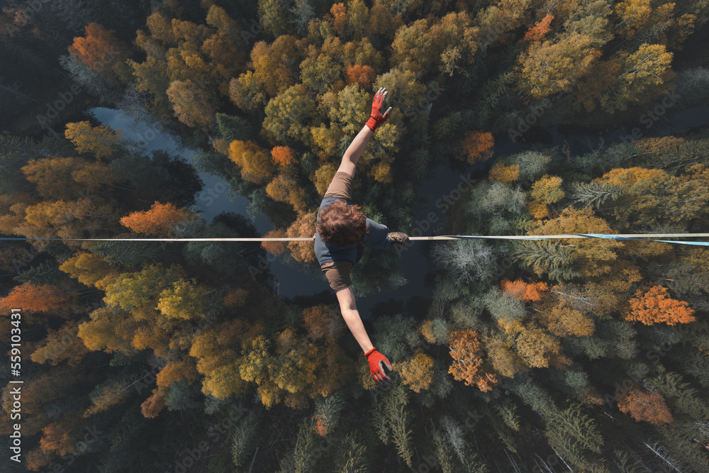 Highline over the forest. Rope walker walks on a rope at high altitude. Drone view. Slackline theme - obrazy, fototapety, plakaty 