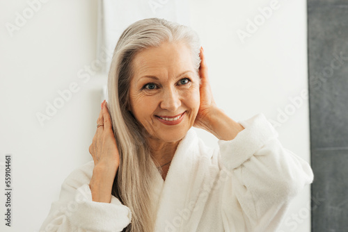фотографія Portrait of a senior woman adjusting her grey hair while looking at the bathroom