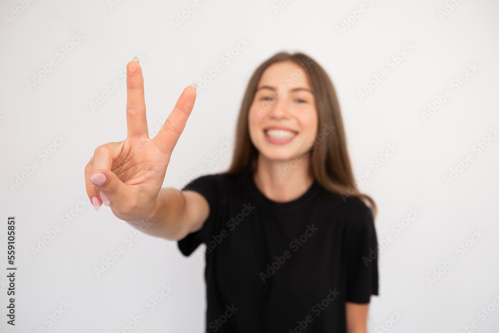 Close-up of female hand making victory gesture over white background. Caucasian lady wearing black T-shirt showing peace sign and smiling. Fun and happiness concept Close-up of female hand making victory gesture over white background. Caucasian lady wearing black T-shirt showing peace sign and smiling. Fun and happiness concept