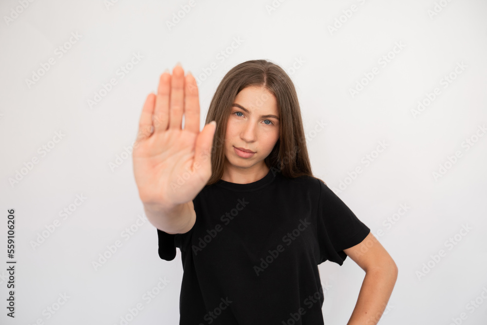 Portrait of confident young woman making stop gesture over white background. Caucasian lady wearing black T-shirt showing forbiddance sign. Restriction concept Portrait of confident young woman making stop gesture over white background. Caucasian lady wearing black T-shirt showing forbiddance sign. Restriction concept
