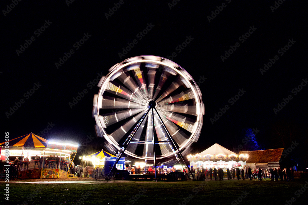 One Ferris wheel and 3 enigmatic rides running at full speed in the dark, at a funfair in Bokrijk in Limburg, Belgium.