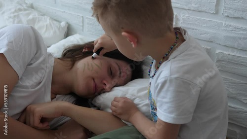 Little naughty charming boy draws markers on the face of a sleeping mom. photo