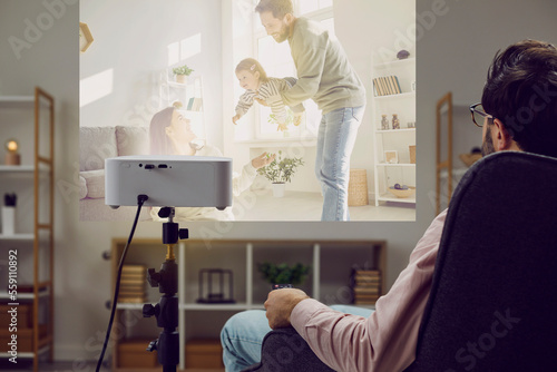 Young man sitting in an armchair at home  watching a good family movie  looking at family photos and videos on a modern projector  relaxing  and enjoying leisure time