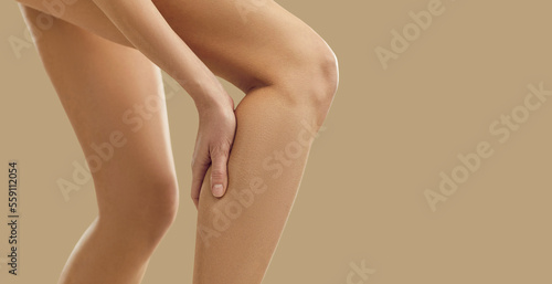 Woman feeling sudden pain in her leg. Young lady has a leg cramp and touches her calf. Female patient suffering from pain due to injured, torn, overstretched muscle. Injury concept. Copy space banner © Studio Romantic