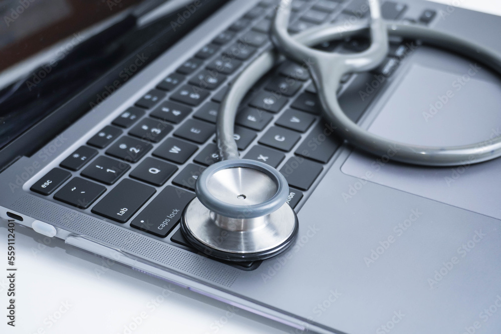 grey Stethoscope on laptop or on the keyboard of pc, close-up. macro view of a grey stethoscope on a business office laptop keyboard with selective focusing effect grey Stethoscope on laptop or on the keyboard of pc, close-up. macro view of a grey stethoscope on a business office laptop keyboard with selective focusing effect
