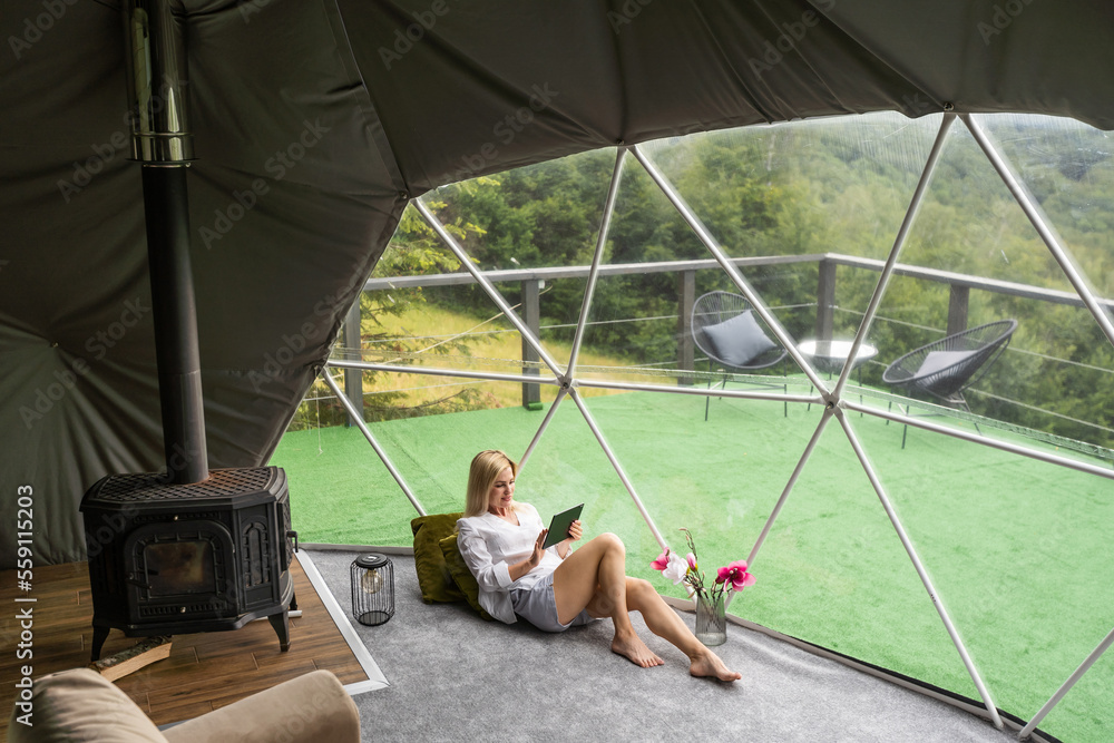 A woman sits in a geo dome glamping tent, looks at the nature.