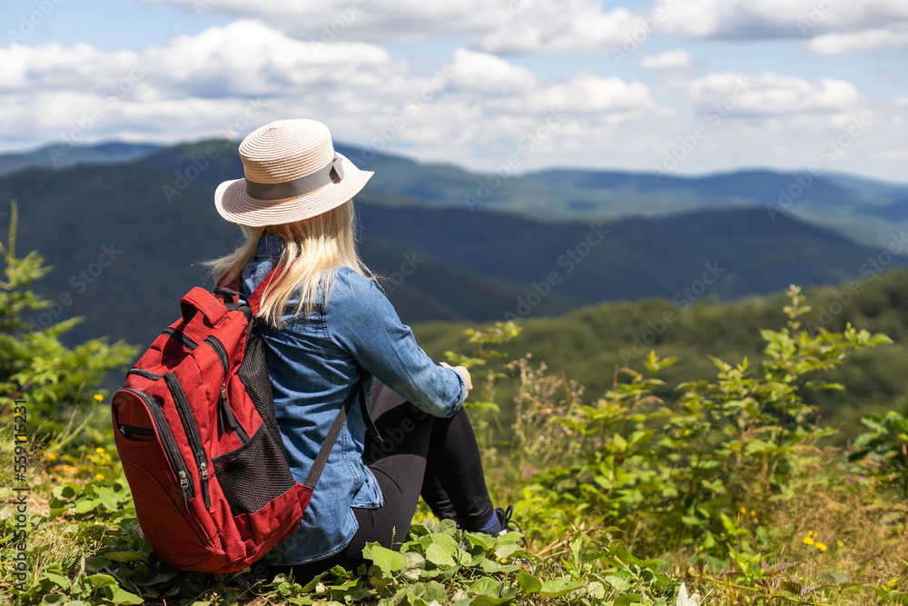 Young woman in jeans sitting on the edge and watching an amazing beautiful mountain landscape on day. Concept of travel, camping, outdoor activities Young woman in jeans sitting on the edge and watching an amazing beautiful mountain landscape on day. Concept of travel, camping, outdoor activities