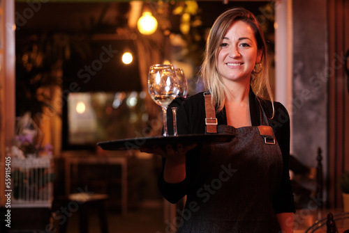 Waitress looking at the camera and smiling while holding a tray with wine glasses.