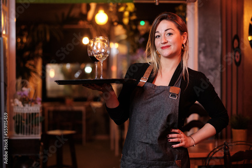 Waitress holding a tray with wine glasses while standing in a restaurant. photo