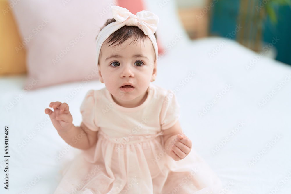 Adorable toddler sitting on bed with relaxed expression at bedroom Adorable toddler sitting on bed with relaxed expression at bedroom