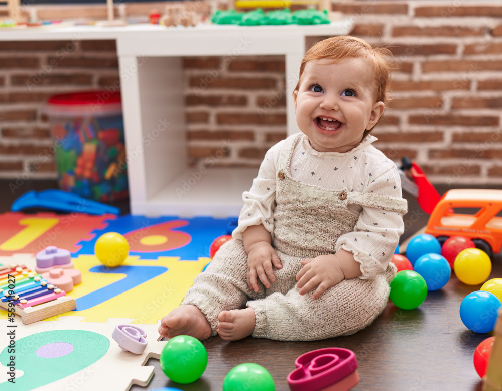Obraz premium Adorable redhead toddler playing with balls sitting on floor at kindergarten
