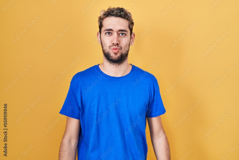 Hispanic man with beard standing over yellow background looking at the camera blowing a kiss on air being lovely and sexy. love expression. Hispanic man with beard standing over yellow background looking at the camera blowing a kiss on air being lovely and sexy. love expression.