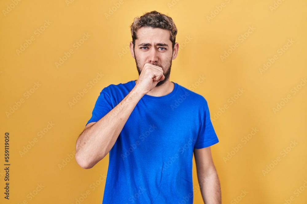 Hispanic man with beard standing over yellow background feeling unwell and coughing as symptom for cold or bronchitis. health care concept. Hispanic man with beard standing over yellow background feeling unwell and coughing as symptom for cold or bronchitis. health care concept.