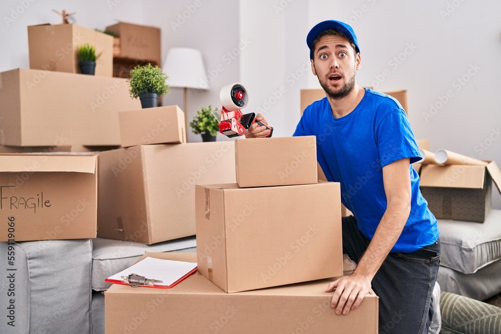 Hispanic man with beard working moving boxes scared and amazed with open mouth for surprise, disbelief face Hispanic man with beard working moving boxes scared and amazed with open mouth for surprise, disbelief face