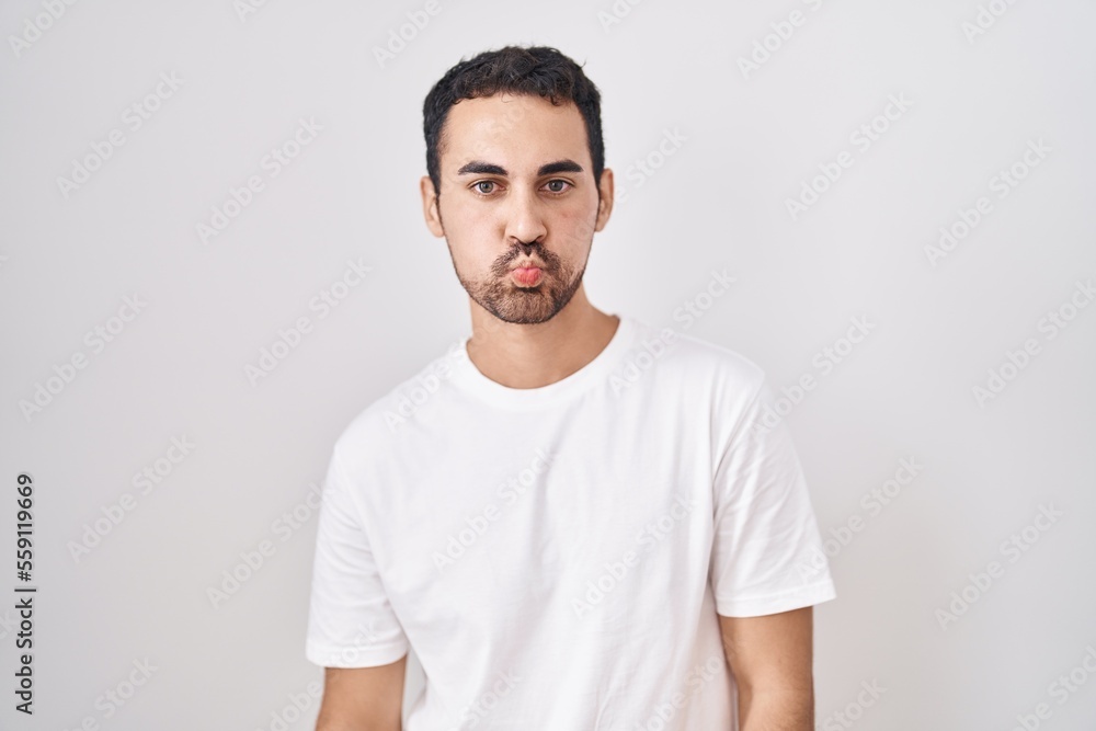 Handsome hispanic man standing over white background puffing cheeks with funny face. mouth inflated with air, crazy expression. Handsome hispanic man standing over white background puffing cheeks with funny face. mouth inflated with air, crazy expression.