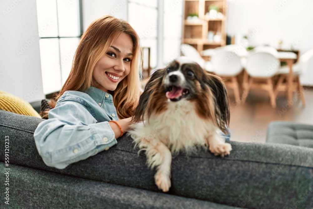 Young caucasian woman smiling confident sitting on sofa with dog at home