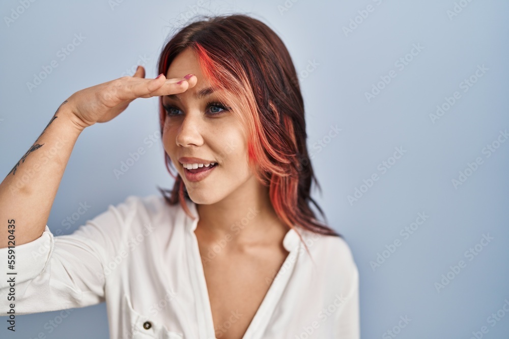 Young caucasian woman wearing casual white shirt over isolated background very happy and smiling looking far away with hand over head. searching concept.