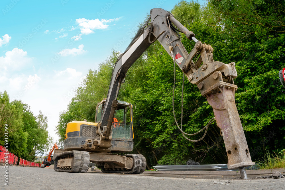 Excavator with hydraulic jack hammer breaking asphalt in preparation for drainage works close up and selective focus Excavator with hydraulic jack hammer breaking asphalt in preparation for drainage works close up and selective focus