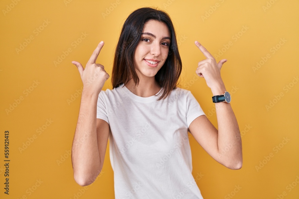 Young beautiful woman standing over yellow background smiling pointing to head with both hands finger, great idea or thought, good memory Young beautiful woman standing over yellow background smiling pointing to head with both hands finger, great idea or thought, good memory