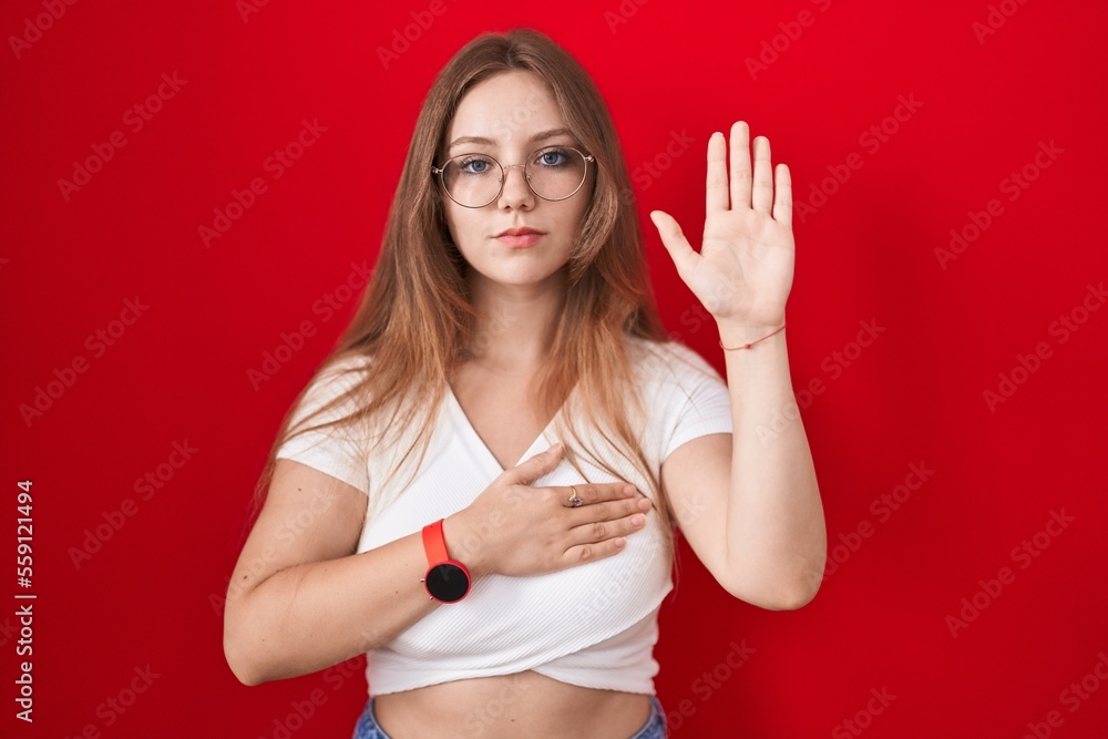 Young caucasian woman standing over red background swearing with hand on chest and open palm, making a loyalty promise oath Young caucasian woman standing over red background swearing with hand on chest and open palm, making a loyalty promise oath