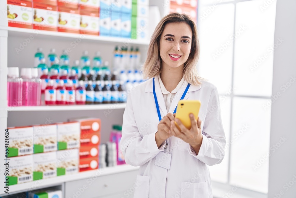 Young woman pharmacist smiling confident using smartphone at pharmacy