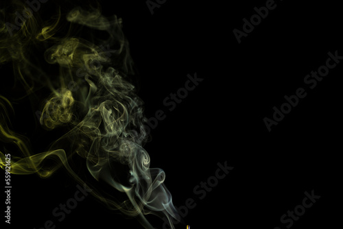 incense stick with yellow green smoke against black background