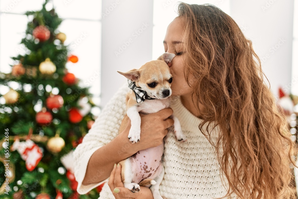 Young beautiful hispanic woman kissing chihuahua standing by christmas tree at home Young beautiful hispanic woman kissing chihuahua standing by christmas tree at home