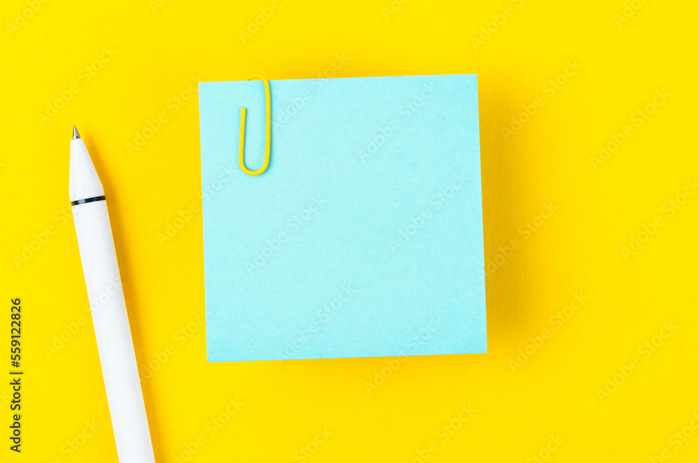 A blank blue notes paper and pen with a paper clip on yellow background, for your text or message. A blank blue notes paper and pen with a paper clip on yellow background, for your text or message.