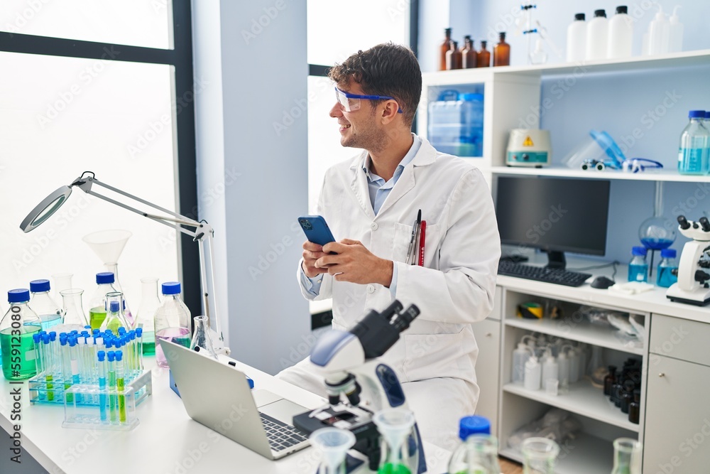 Obraz premium Young hispanic man scientist smiling confident using smartphone at laboratory