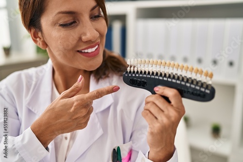 Young latin woman wearing dentist uniform holding whitening test at clinic