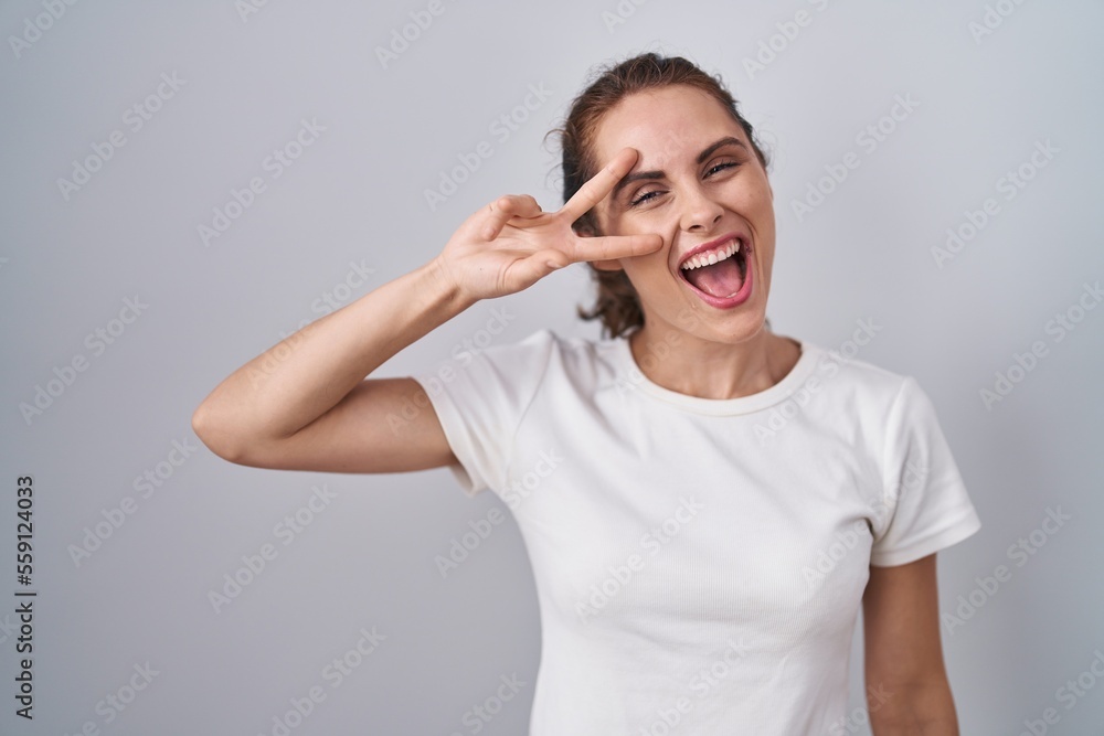 Beautiful brunette woman standing over isolated background doing peace symbol with fingers over face, smiling cheerful showing victory Beautiful brunette woman standing over isolated background doing peace symbol with fingers over face, smiling cheerful showing victory