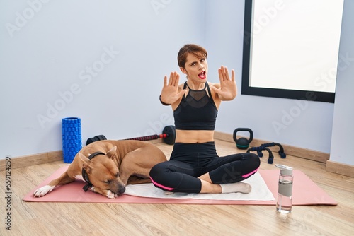 Young beautiful woman sitting on yoga mat doing stop gesture with hands palms, angry and frustration expression